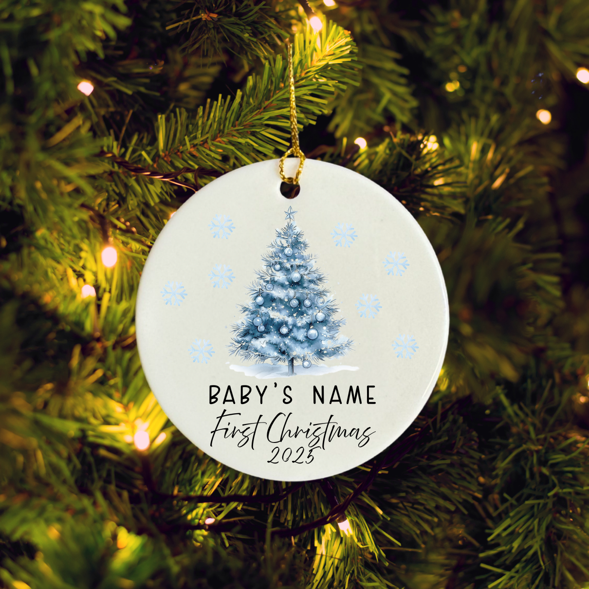 Round Christmas ornament with a tree design and 'Baby's Name First Christmas 2025' text, hanging on a lit Christmas tree.