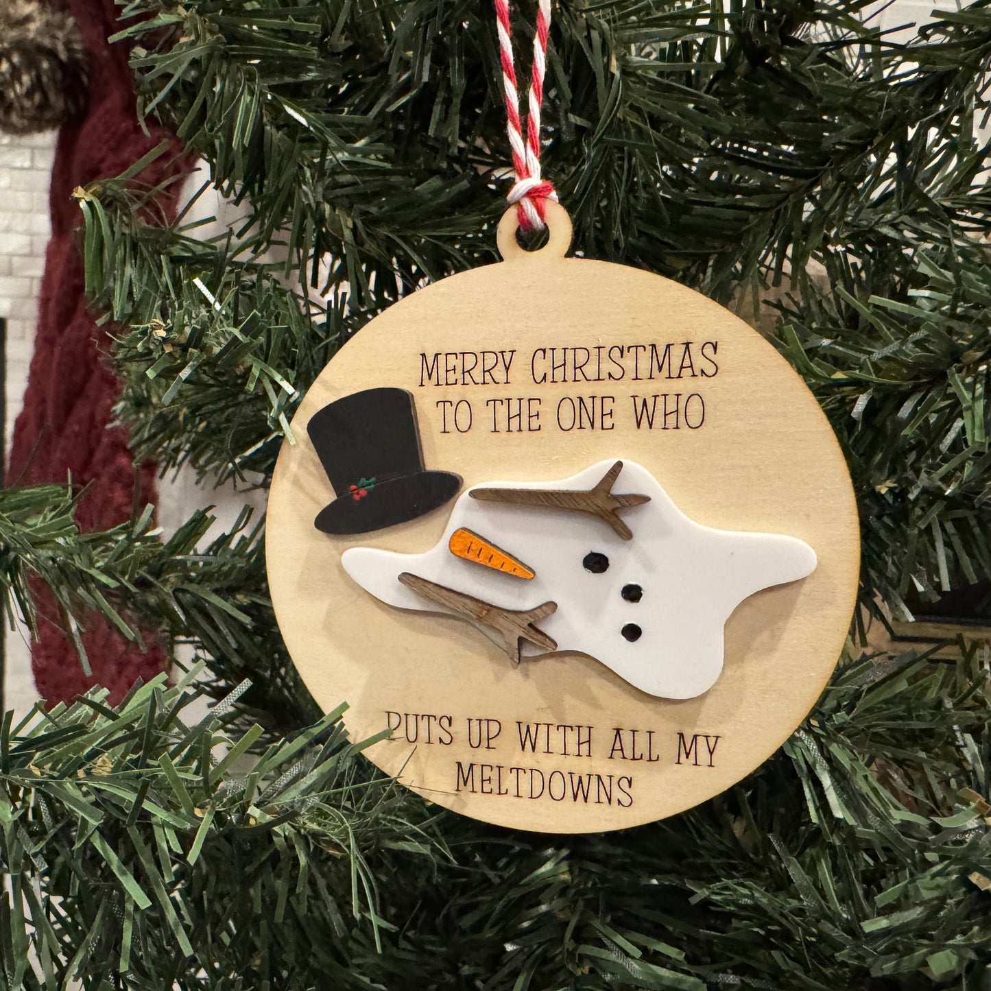 Wooden Christmas ornament with snowman design and text on a tree.