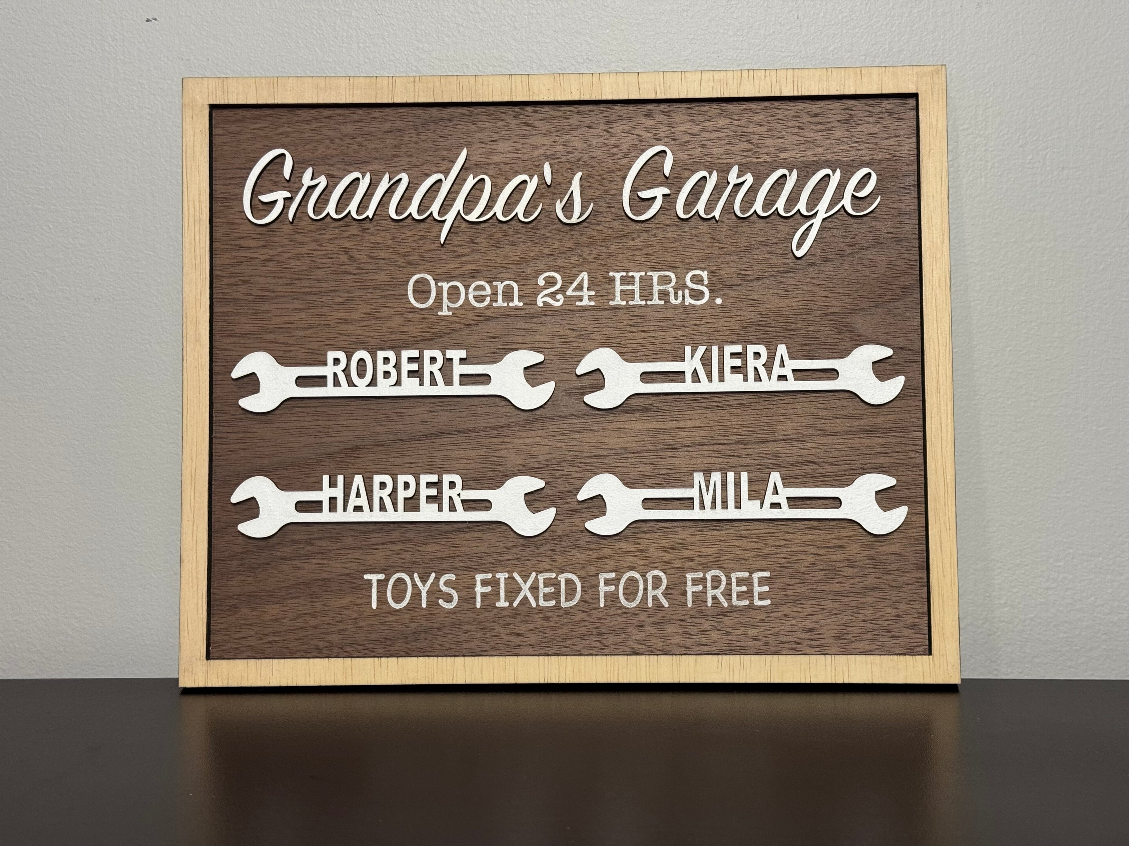 Wooden sign with names on wrenches and humorous text about 'Grandpa's Garage' on a gray background.