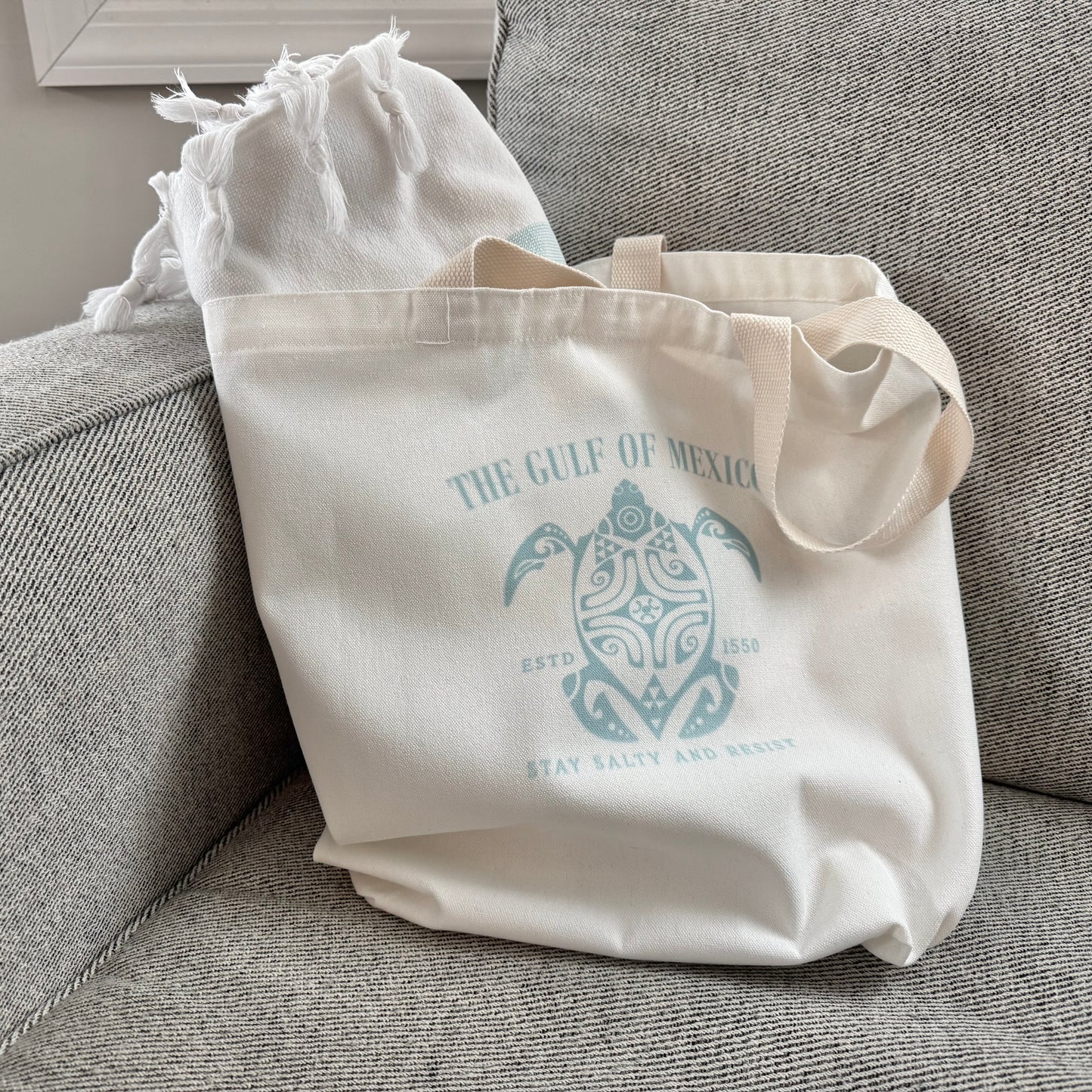 Beige tote bag with turtle design and text on a gray couch