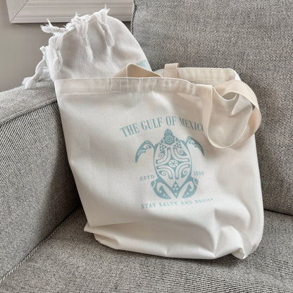 Beige tote bag with turtle design and text on a gray couch