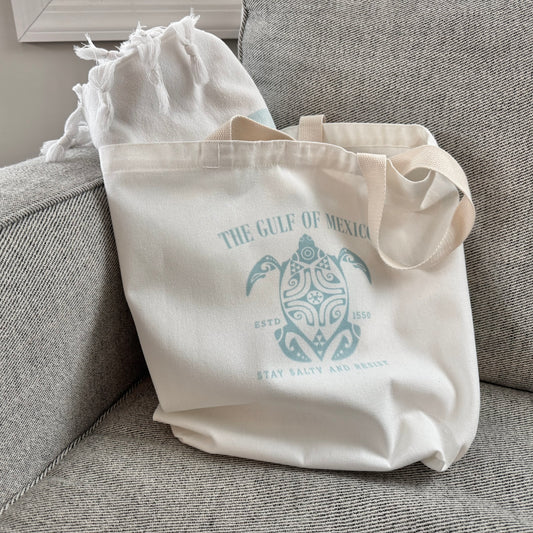 Beige tote bag with turtle design and text on a gray couch