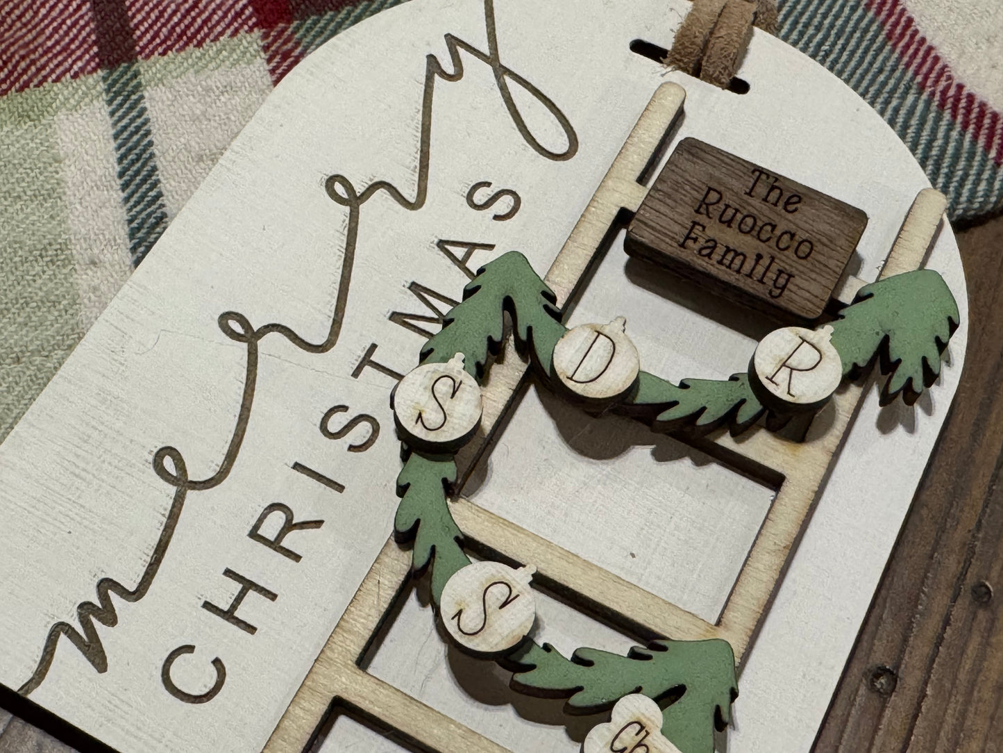 Wooden Christmas ornament with 'Merry Christmas' and family name on a plaid fabric background