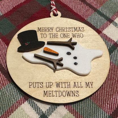 Decorative Christmas ornament with a snowman design and humorous text on a plaid fabric background.