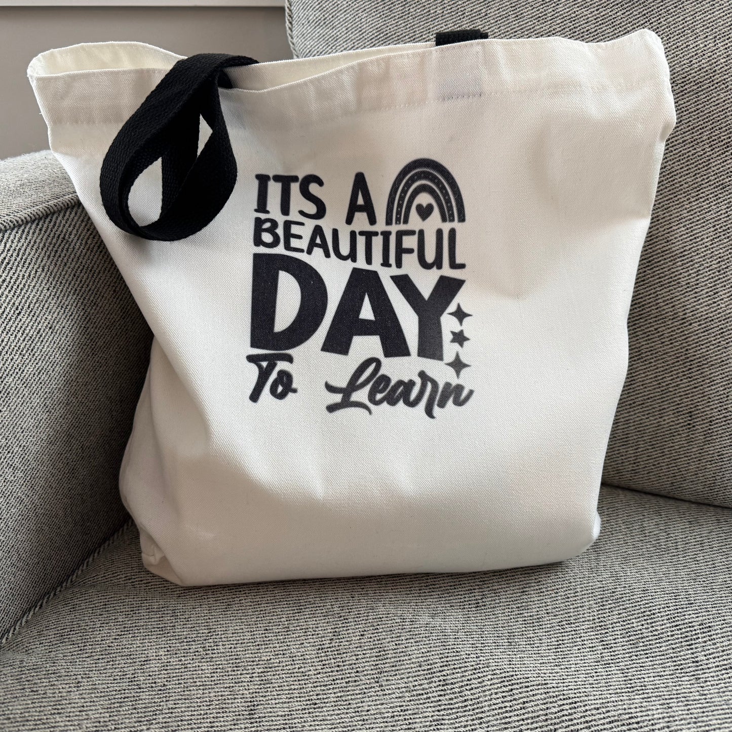 tote bag with 'It's a Beautiful Day to Learn' text on a gray couch.