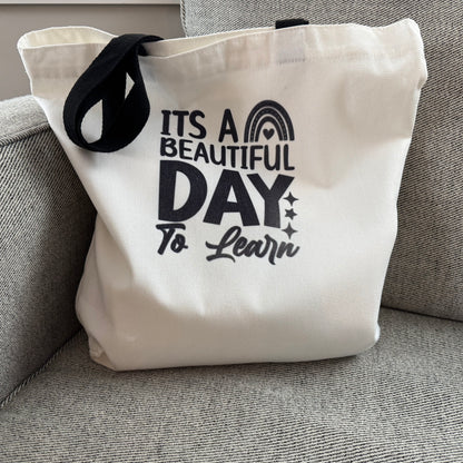 tote bag with 'It's a Beautiful Day to Learn' text on a gray couch.