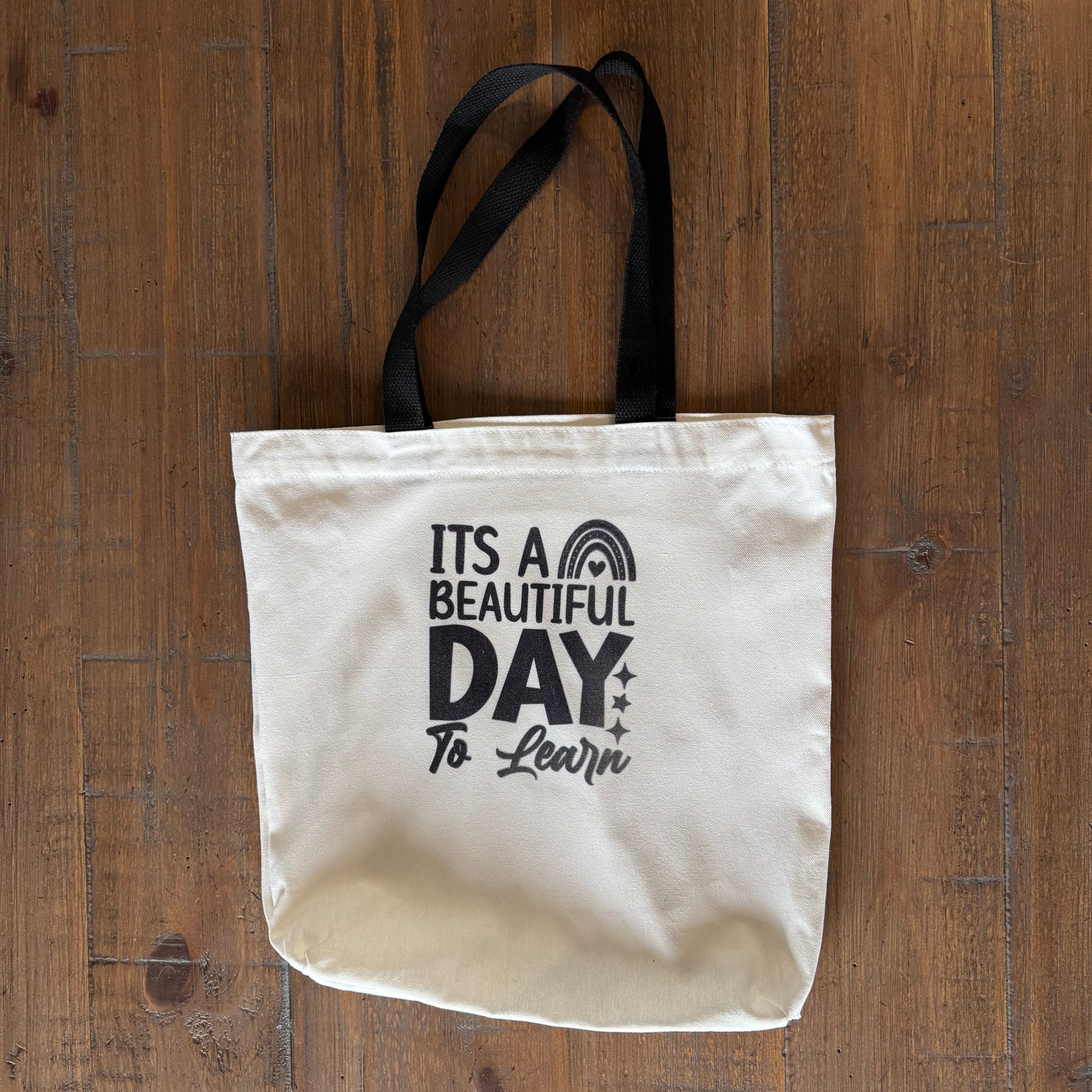 tote bag with 'It's a Beautiful Day to Learn' text on a wooden surface