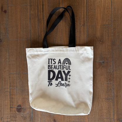 tote bag with 'It's a Beautiful Day to Learn' text on a wooden surface