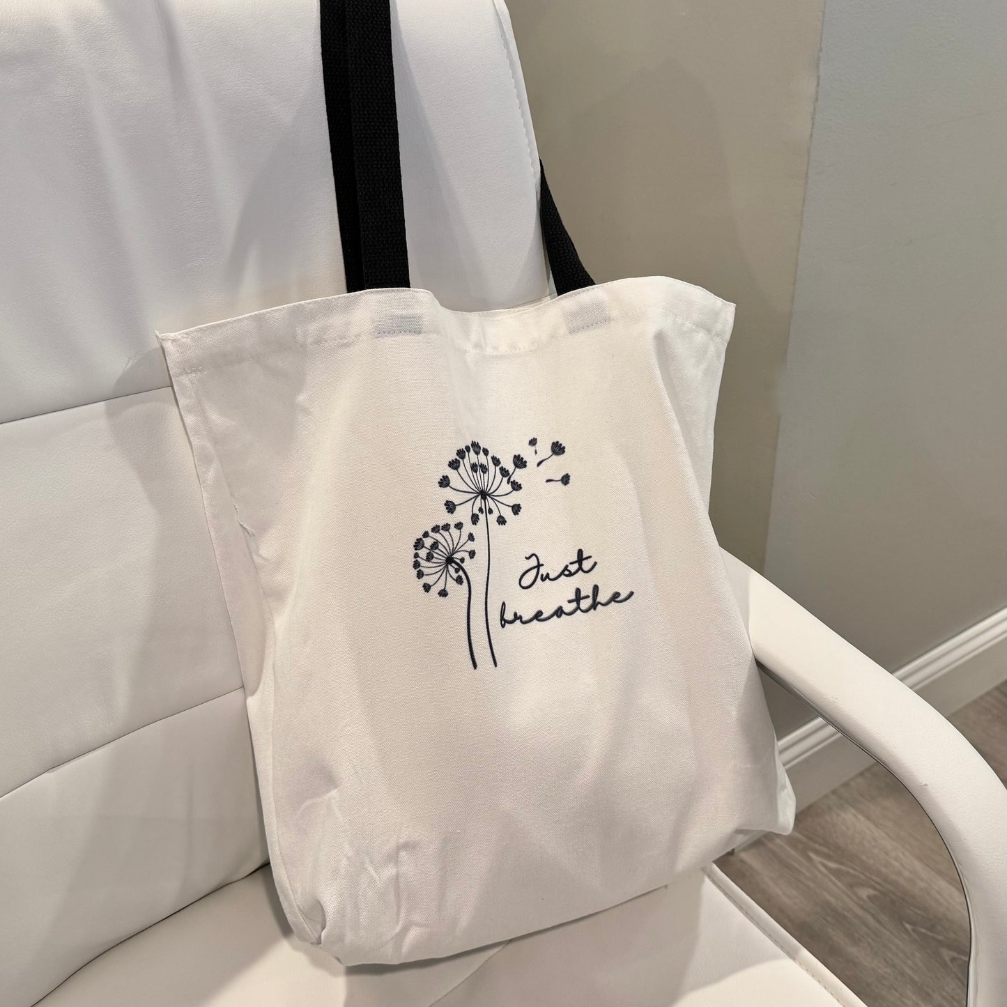 tote bag with a dandelion design and 'Just Breathe' text on a chair.