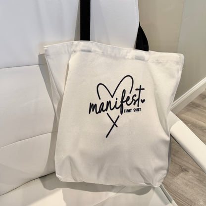 tote bag with 'manifest that shit' text on a white chair.