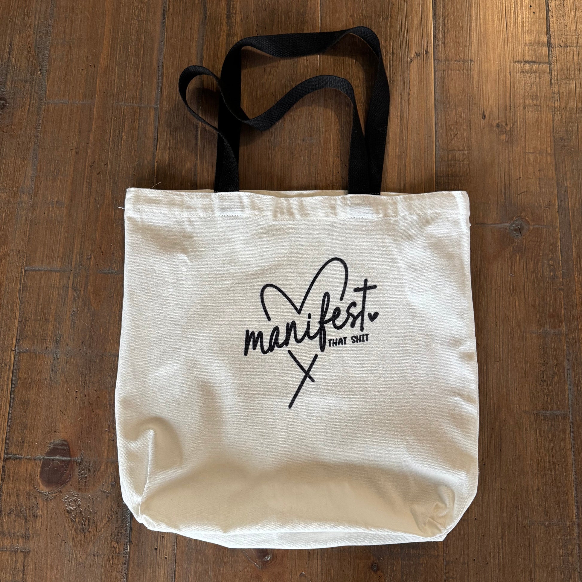 White tote bag with 'manifest' branding on a wooden surface