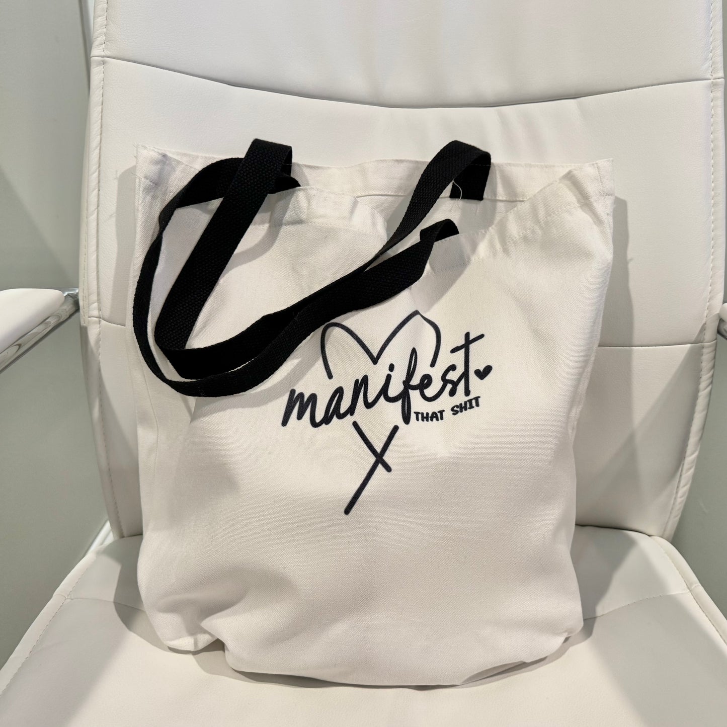 tote bag with black graphic and handles on a white chair