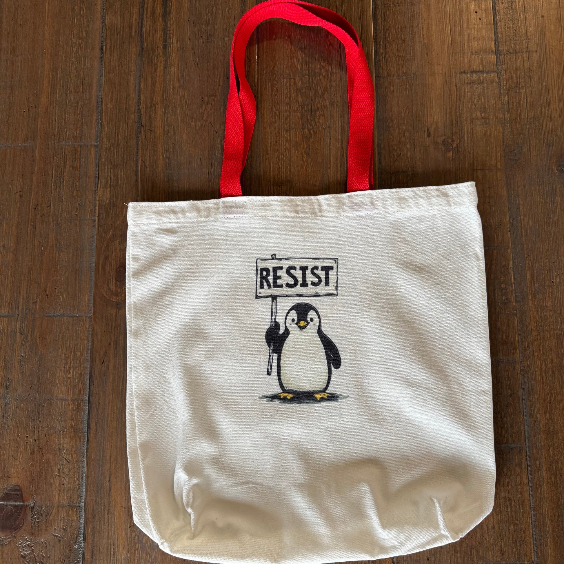 Tote bag with a penguin holding a 'RESIST' sign on a wooden surface