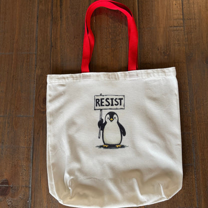 Tote bag with a penguin holding a 'RESIST' sign on a wooden surface