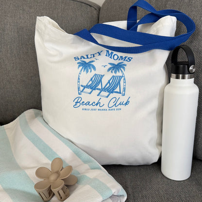 Lifestyle photo of tote bag with blue text and graphics, white water bottle, and striped towel on a gray surface.