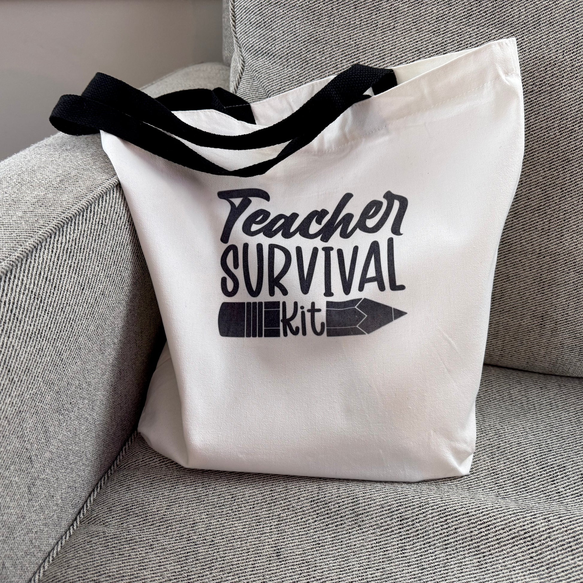 Tote bag with 'Teacher Survival Kit' text on a gray couch