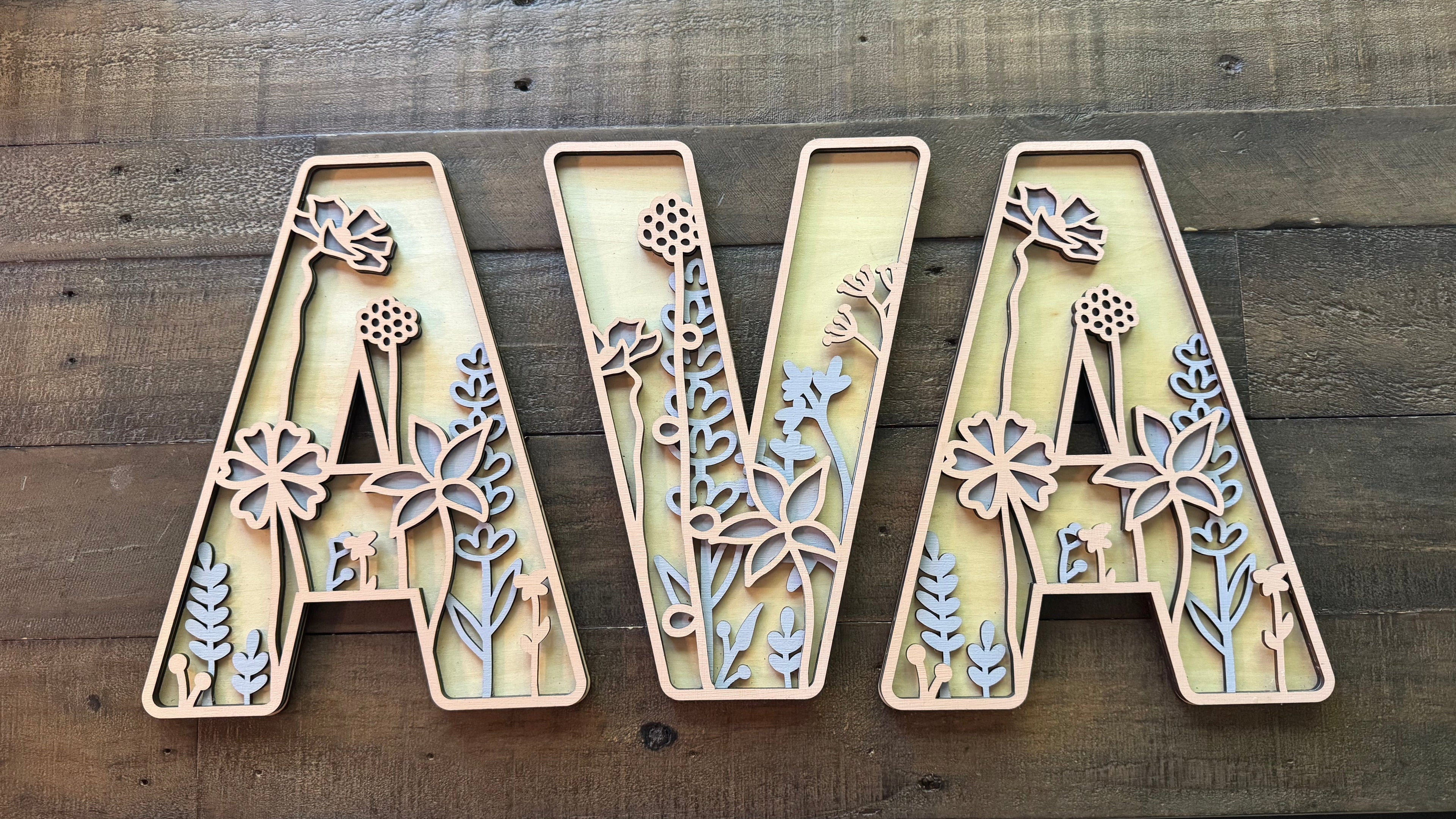 Wooden letters spelling 'AVA' with floral designs on a wooden surface